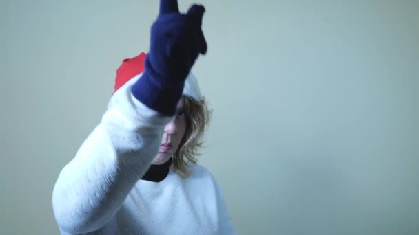 Взрослая сорокалетняя блондинка в красной новогодней шляпе показывает пальцем вперед. Портрет медленного движения. Новый год. Веселые Рождества - Кадры, видео