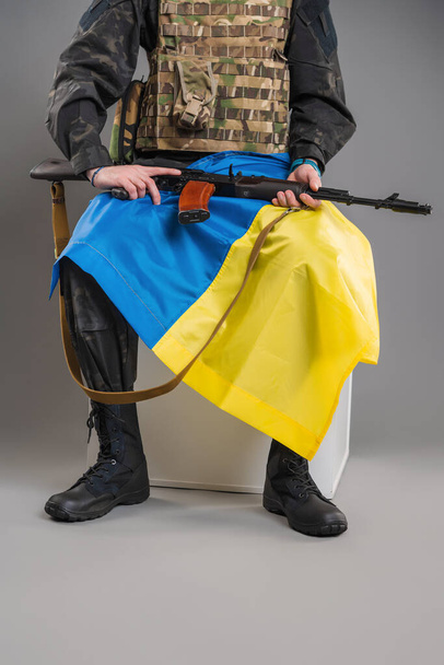 A soldier sits with a weapon and with a Ukrainian flag on his hands - Fotografie, Obrázek