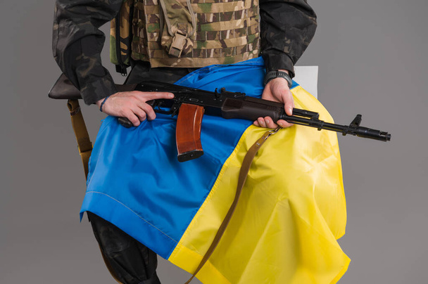 A soldier sits with a weapon and with a Ukrainian flag on his hands - Фото, зображення