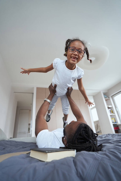 Дорослі афроамериканці тримають дочку над собою в ліжку. - Фото, зображення