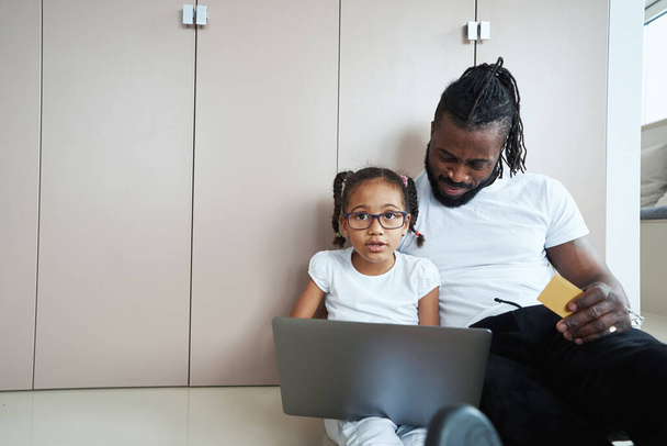 Tochter sitzt neben Vater mit Laptop auf Schoß - Foto, Bild