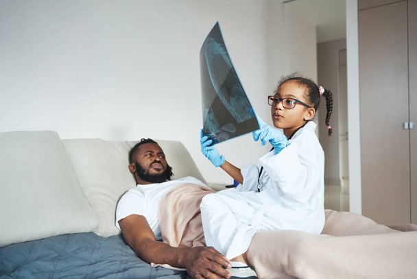 African American girl in medical gown examining her fathers x-ray - Фото, изображение