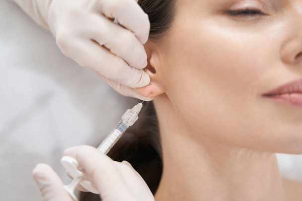 Doctor beautician making beauty injection in female ear - 写真・画像