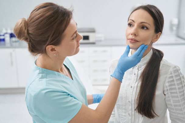 Лікар перевіряє шкіру обличчя жінки в косметологічній клініці
 - Фото, зображення