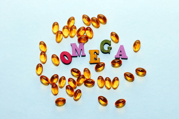 Fish oil tablets in a golden jelly shell with the letters Omega on a light background. - Foto, Imagen