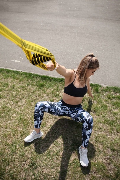 Attractive woman training on TRX outdoors, morning workout. Adult healthy fitness. - Foto, imagen