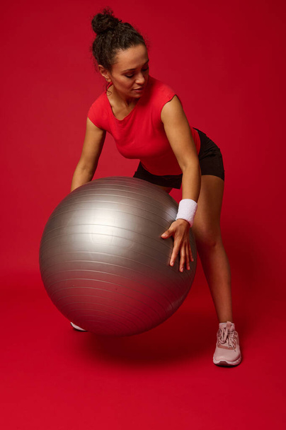 Middle aged African American sporty woman exercising with fitness ball against red background with copy ad space for advertising text - Photo, image