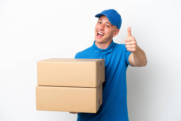 Young delivery Brazilian man isolated ops white background with thumbs up because something good has happened - Photo, Image