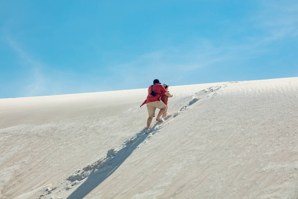 father helps his son up a sand dune in desert - Foto, imagen