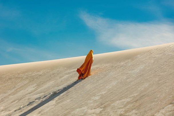 woman in yellow arabic clothing climbing a dune in the desert - Zdjęcie, obraz