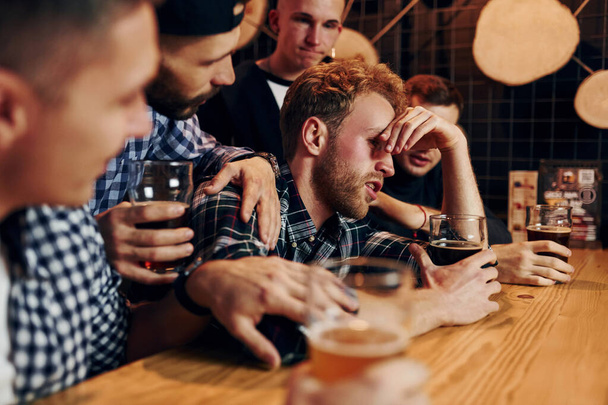 Sad man feels bad. Group of people together indoors in the pub have fun at weekend time. - Fotó, kép