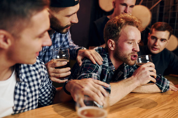 Sad man feels bad. Group of people together indoors in the pub have fun at weekend time. - Foto, Bild
