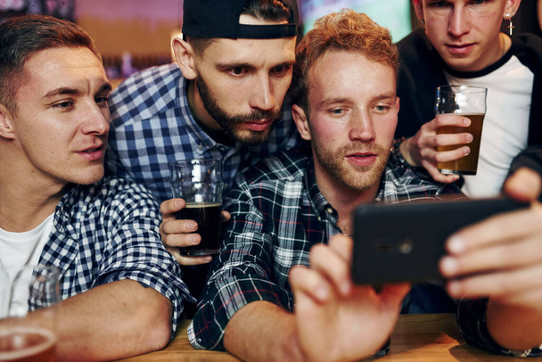 Uses phone. Group of people together indoors in the pub have fun at weekend time. - Foto, imagen