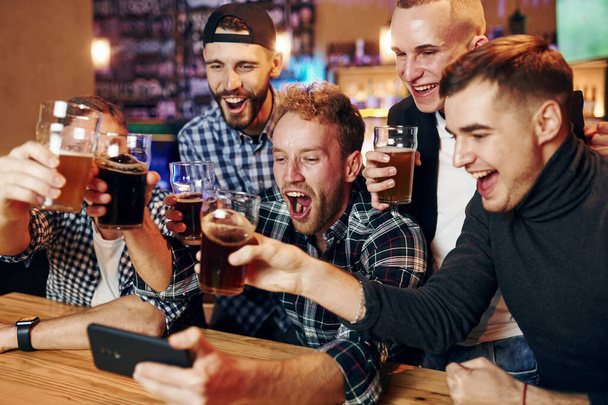 Uses phone. Group of people together indoors in the pub have fun at weekend time. - Foto, afbeelding