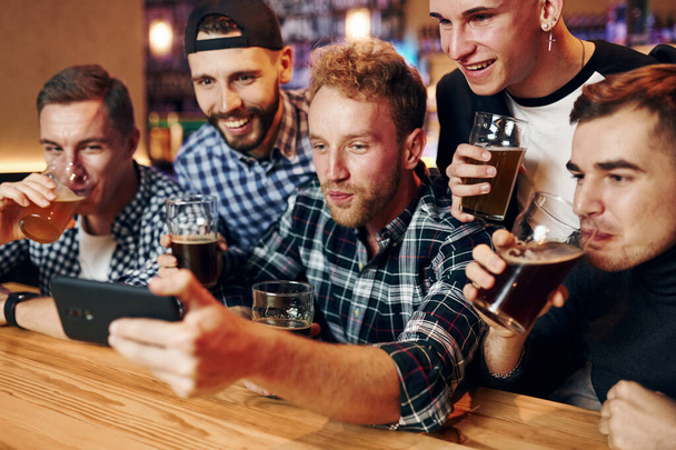 Uses phone. Group of people together indoors in the pub have fun at weekend time. - Photo, image