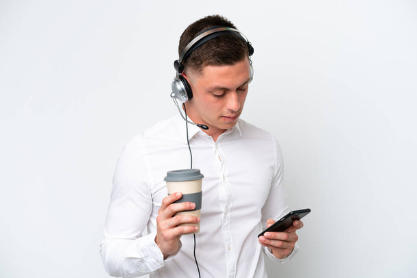 Бразилець працює з навушником на білому фоні, тримаючи каву і мобільний. - Фото, зображення