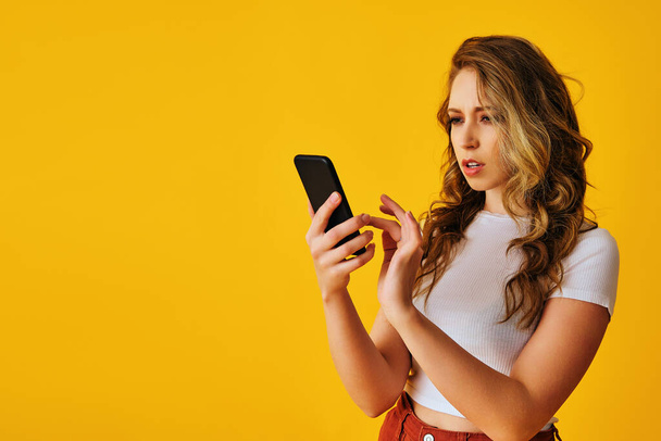 hermosa mujer joven con teléfono inteligente y teléfono móvil sobre fondo amarillo - Foto, Imagen