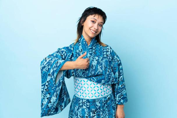 Νεαρή γυναίκα φορώντας κιμονό πάνω από απομονωμένο μπλε φόντο δίνοντας ένα αντίχειρες επάνω χειρονομία - Φωτογραφία, εικόνα