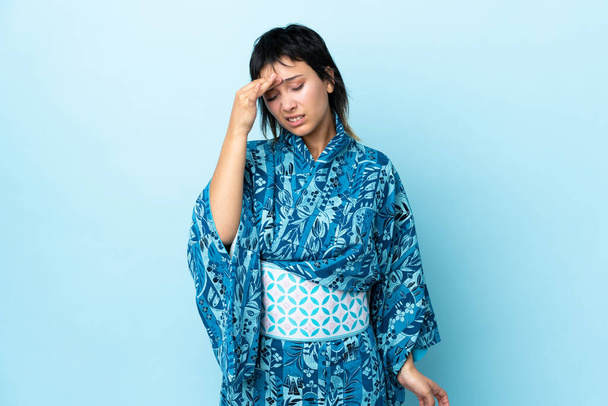 Молодая женщина в кимоно на изолированном синем фоне с головной болью - Фото, изображение