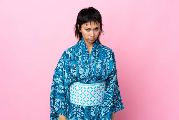 jonge vrouw dragen kimono over geïsoleerde blauwe achtergrond met trieste uitdrukking - Foto, afbeelding