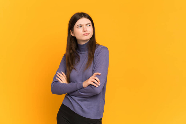 Young Ukrainian girl isolated on yellow background making doubts gesture while lifting the shoulders - 写真・画像