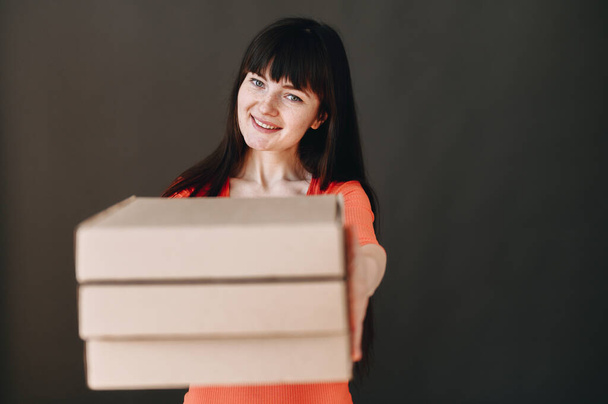 A young girl holds pizza boxes in her hands and sincerely smiles looking up. Girl on a gray background in a bright dress. pizza delivery concept. - Photo, Image