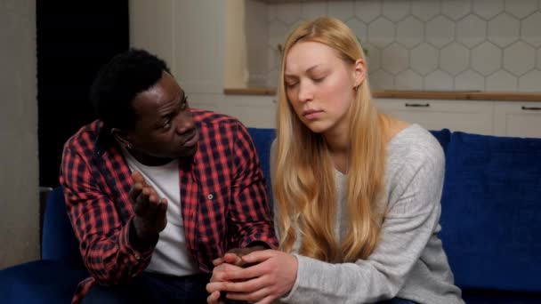 African American man calms caucasian upset woman sitting on couch at home - Πλάνα, βίντεο