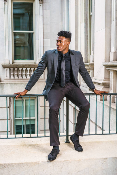 African American Businessman working in New York, wearing fashionable jacket, black necktie, wristwatch, sitting on railing in vintage style office building, taking break - Foto, afbeelding