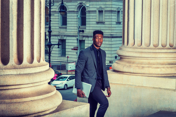 Uomo d'affari afroamericano che viaggia, lavora a New York, indossa giacca alla moda, cravatta, trasporta computer portatili, entra in un palazzo di uffici vintage dalla strada. effetto filtrato - Foto, immagini