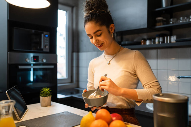 Una joven mujer caucásica desayunando en la cocina en casa mujer adulta comiendo en su apartamento mientras está de pie teniendo comida vegana saludable muesly o avena sonrisa feliz gente real copiar espacio - Foto, imagen