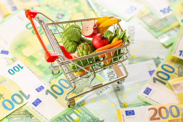 Ceny żywności w Europie. Kosz spożywczy w Europie.kryzys żywności.wózek sklepowy z artykułami spożywczymi na tle banknotów euro.Kosz żywnościowy w strefie euro - Zdjęcie, obraz