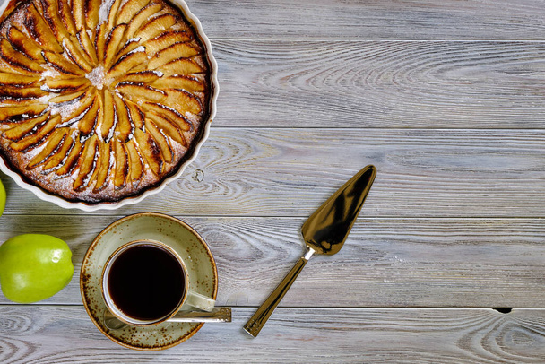 Torta perfumada com maçãs em forma de cerâmica branca para assar em uma velha mesa de madeira com uma xícara de café preto. Comida saborosa e saudável. - Foto, Imagem