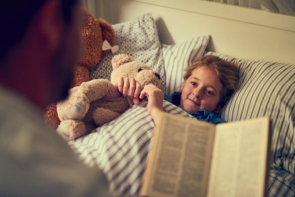 いくつかの甘い夢をスパークさせる魔法の物語。自宅で彼の小さな娘に就寝前の話を読んでいる父親の作物のショット. - 写真・画像