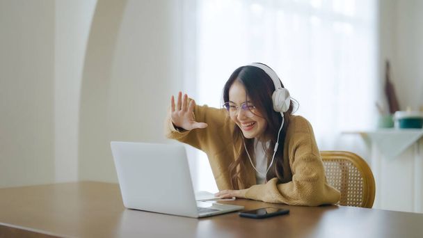 家のコンピュータのラップトップで働いている眼鏡とヘッドセットを身に着けている若いアジアの女性。自宅で働く,ビデオ会議,ビデオ通話,学生オンラインクラスを学ぶ - 写真・画像