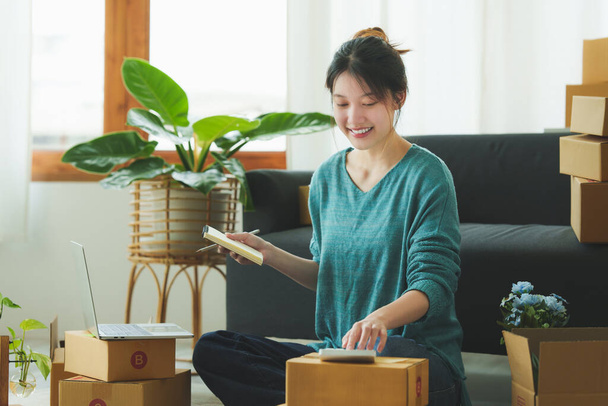 Een portret van een Aziatische vrouw, e-commerce medewerker freelance met pakketdoos voor levering aan de klant. Online marketing verpakking doos levering concept. - Foto, afbeelding