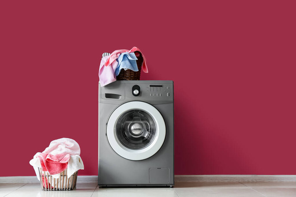 Modern washing machine with laundry baskets near red wall - Foto, afbeelding