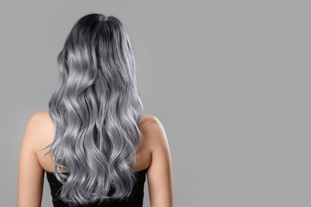Beautiful young woman with dyed hair on grey background, back view - Photo, Image