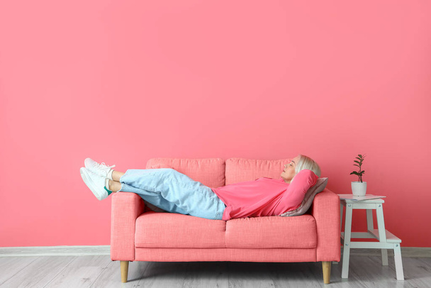 Olgun bir kadın pembe duvarın yanındaki kanepede dinleniyor. - Fotoğraf, Görsel