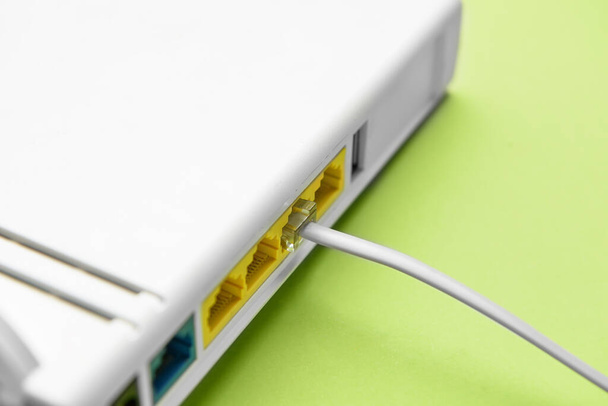 Modern wi-fi router and internet cable on green background, closeup - 写真・画像