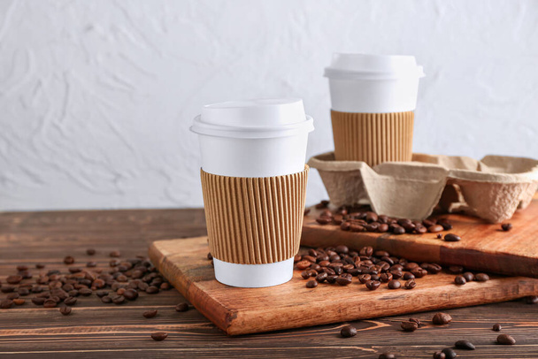 Tazas de papel para llevar y granos de café en la mesa - Foto, imagen