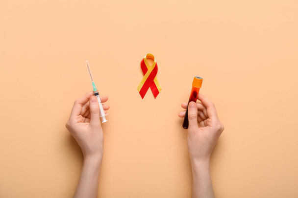 Woman with syringe, blood sample and awareness ribbon on beige background. Hepatitis concept - Фото, изображение