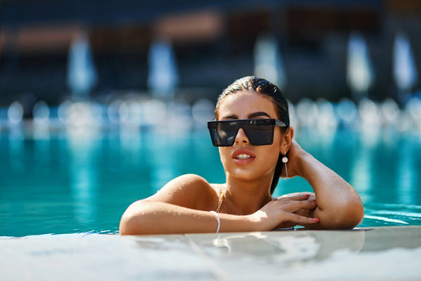Glamorous woman in stylish sunglasses enjoying swimming in turquoise water.  - Фото, зображення