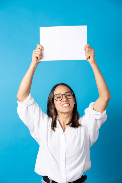 Hispanic pretty woman holding up white board with copy space isolated on blue background. - Foto, immagini
