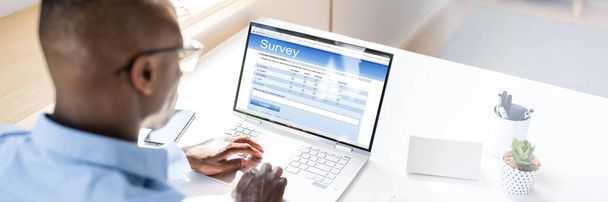 African Man Filling Online Survey Form On Laptop Computer - Foto, imagen