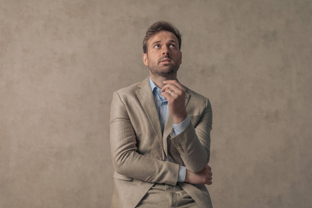attractive businessman folding his arms, looking up and posing with style against wallpaper - Foto, Imagem