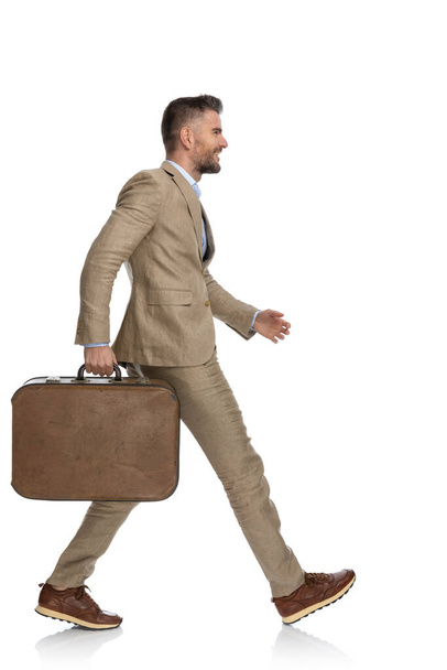 side view of happy businessman with baggage smiling and walking away, going to a work conference in front of white background in studio - Фото, изображение