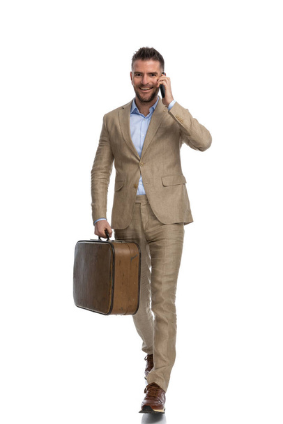 full body picture of attractive young man having a conversation on the phone, leaving town on his free days and smiling on white background in studio - Photo, Image