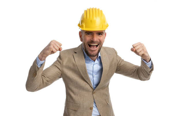 happy engineer guy with helmet holding arms in the air and celebrating project victory on white background - Foto, Imagen