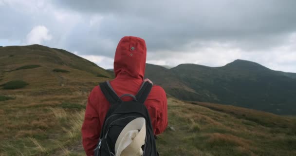 back view, tourist person in a red jacket with a hood and a backpack, looks at the mountains and clouds. Medium shot, daytime, usually spring summer. Carpathians, Ukraine, Europe - Кадри, відео