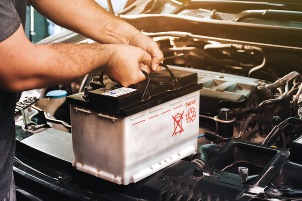 Ein Automechaniker trägt eine Ersatzbatterie für die Wartung des Autos bei sich - Foto, Bild